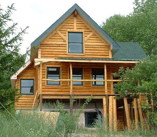 gable end of the log sided house with a covered porch on peeled cedar posts
