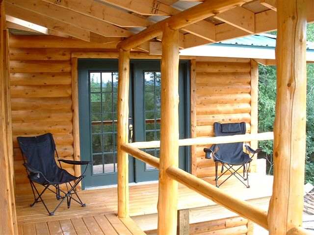 covered deck with peeled cedar posts and rails outside a pair of glass doors