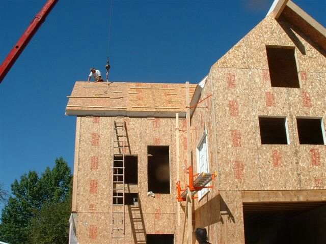 crane lifting a roof panel while two men set it in place on the roof deck