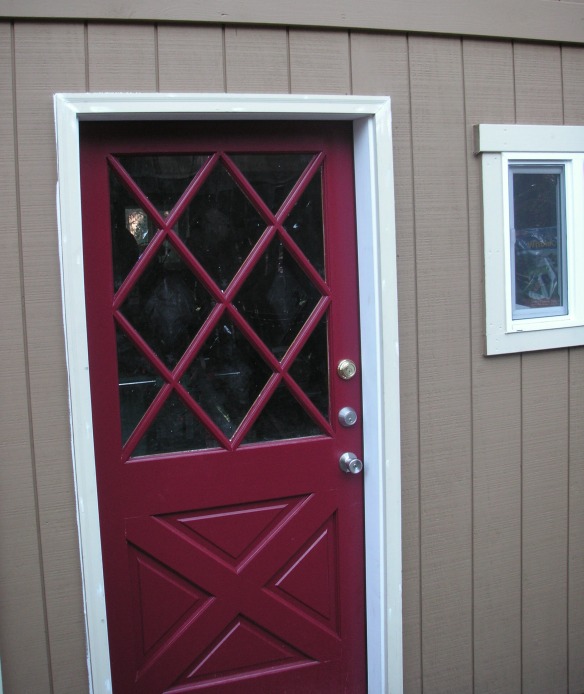 red cross-buck door with a diamond muntin pattern over the glass, in a white painted jamb