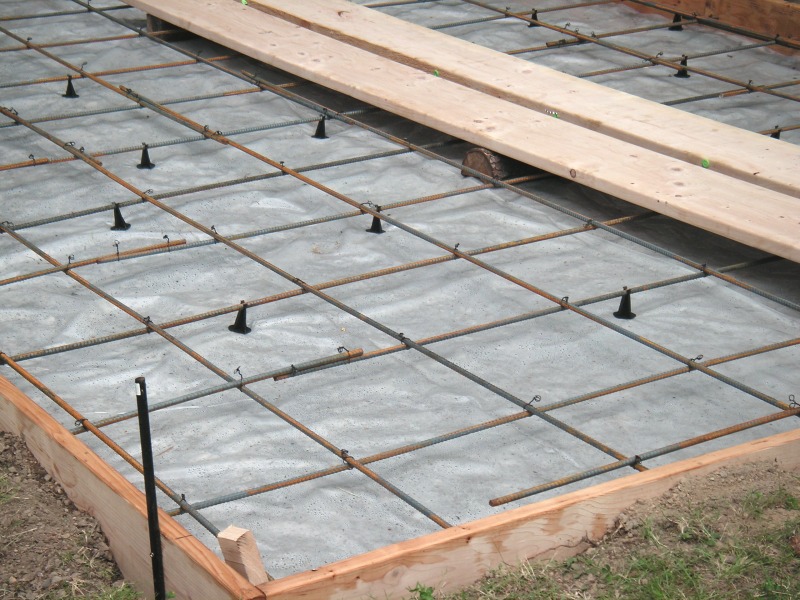 slab on grade foundation ready to pour, with a rebar grid on chairs over plastic sheeting inside wood forms