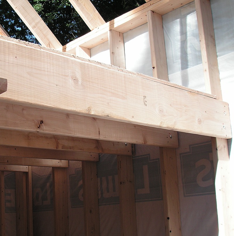 loft floor joists and a rim board bolted through the tall wall studs, with sheathing and housewrap behind