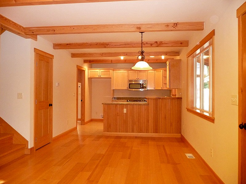 dining area under exposed beams with the kitchen ahead and the stair on the left