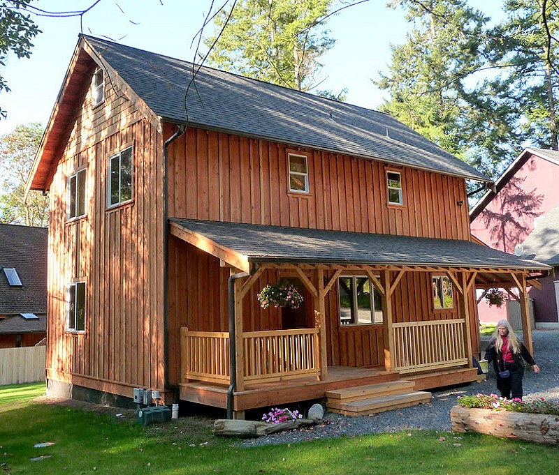 two story cottage with vertical board and batten siding and a covered porch along the long wall