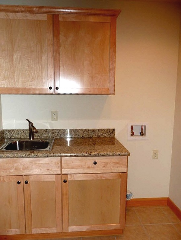utility area with a sink, upper cabinets and an open space with hookups for a stacked washer and dryer