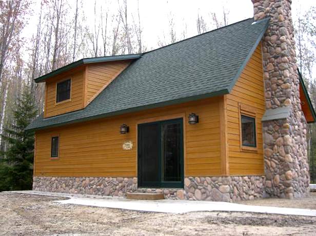 cabin exterior with the river rock chimney and stone base finished, and the shed dormer above the entry door