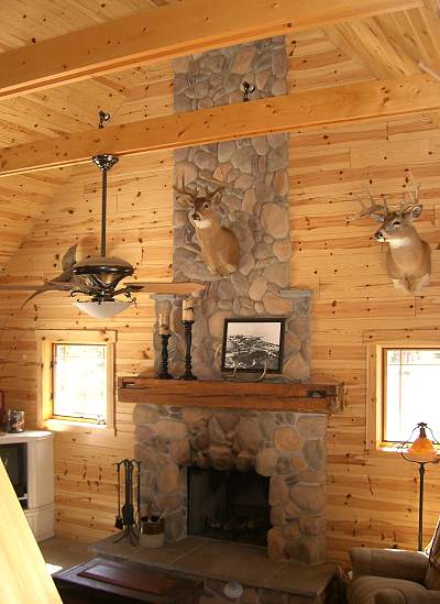 stone fireplace and chimney running up the pine wall to the ceiling, with a reclaimed beam mantel, seen from the loft
