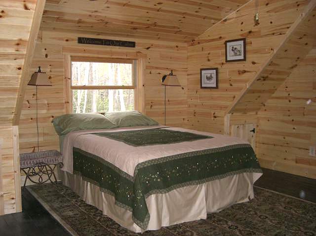 loft bedroom finished in pine, with a bed under the window and the roof sloping down on the right