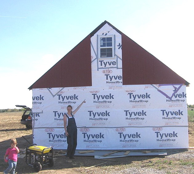 Cody at the gable end wall, siding started above the Tyvek, a small girl running past