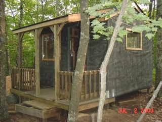 the cabin seen from the front, with dark tarpaper walls and a log railed porch