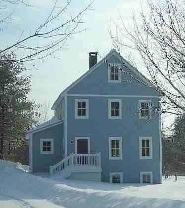 two story house in Maine standing in deep snow, with a small entry porch and steps