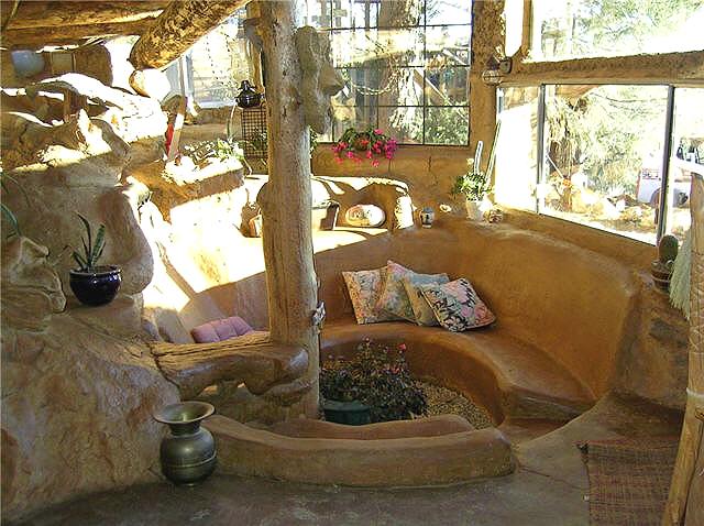the sunken sitting area of the underground hobbit house, with cob benches and cushions