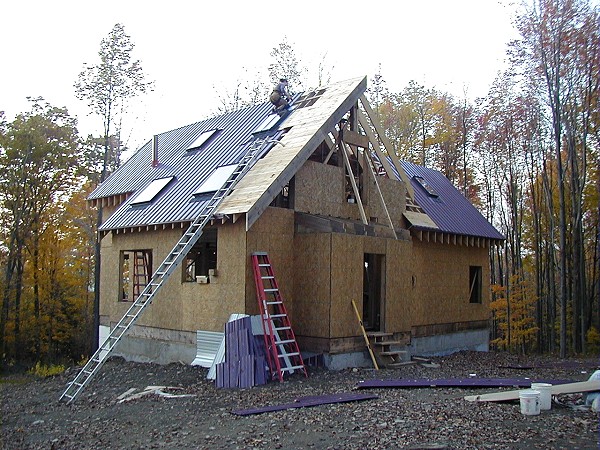 metal roofing going on over the loft framing, with a worker in a safety harness near the ridge