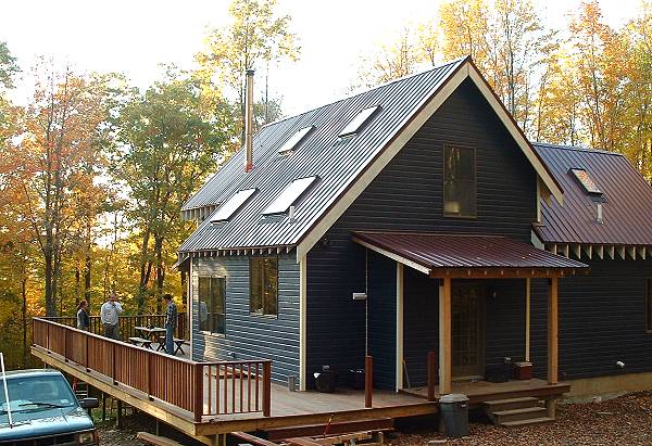 finished two story cottage with dark siding, a standing seam metal roof and a long entry deck