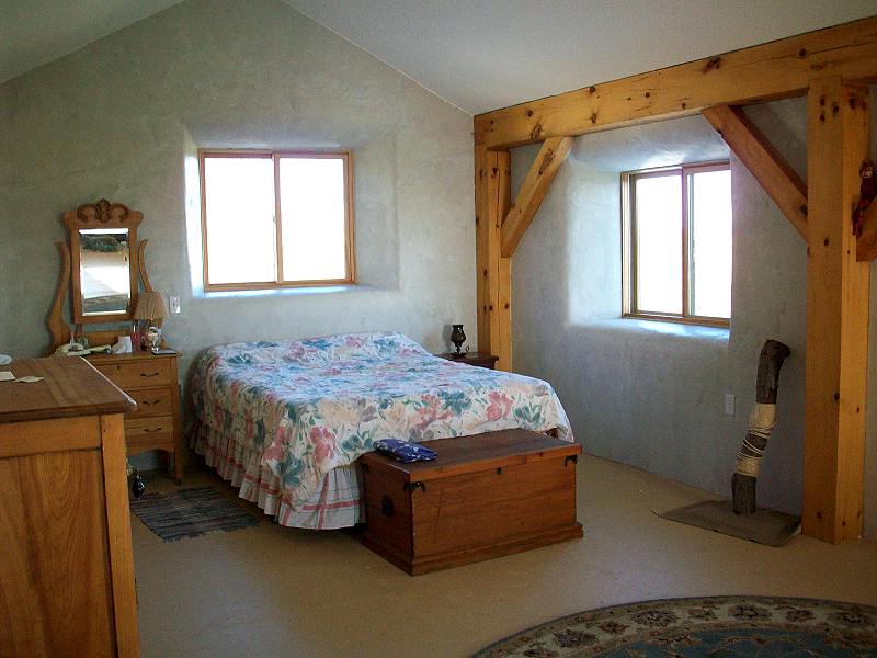 upstairs bedroom with a sloped plastered ceiling, timber posts and deep set windows