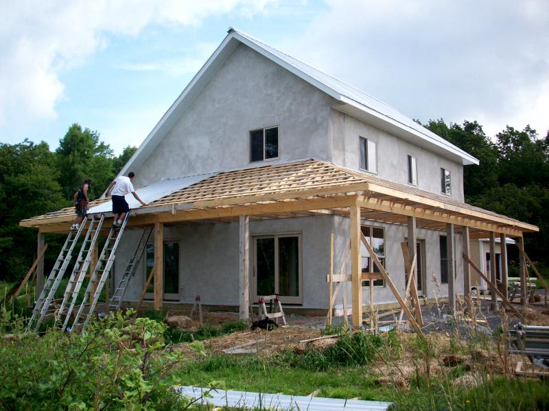 two people laying metal roofing on the porch of the straw bale house during construction