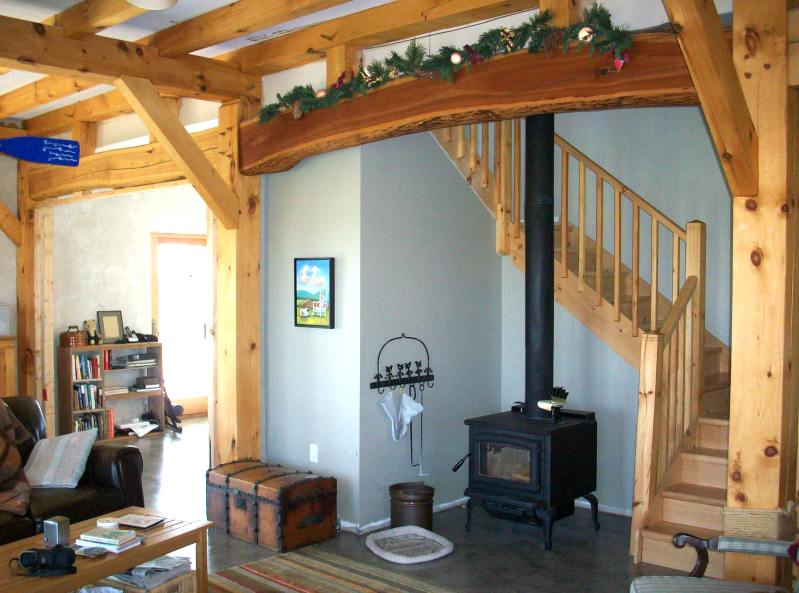 living room with a curved timber frame arch, a woodstove and the stair to the second floor
