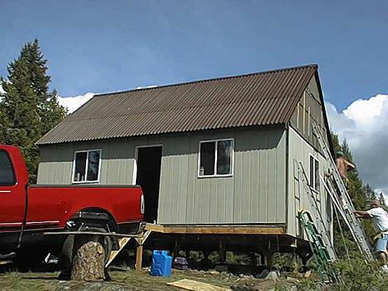 pickup truck backed up to the cabin as the Ondura roofing and siding go on