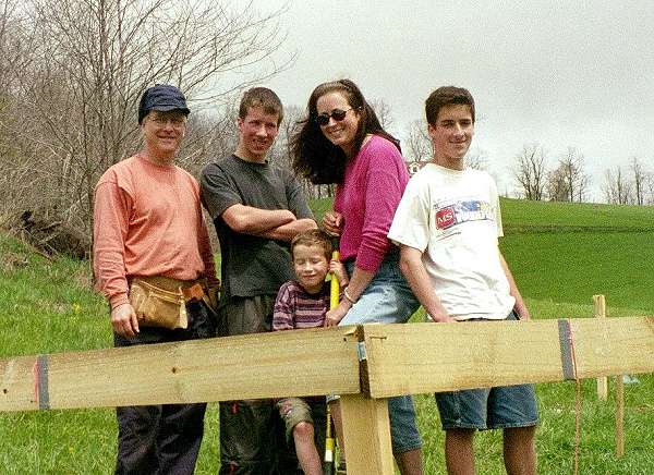 the family of five standing together behind the batter boards at the building site
