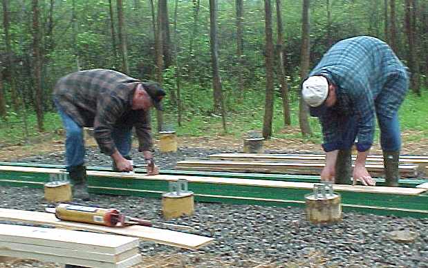 two men bent over a built up beam on the crushed rock, working between the pier tops