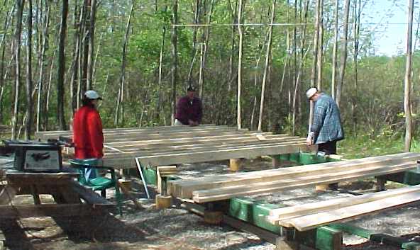three people laying floor joists and decking across the beams, with a chop saw set up at the left