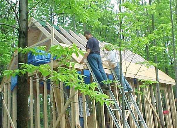 two men on ladders nailing sheathing onto the roof rafters of the framed cabin