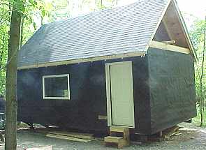 front of the cabin with the door hung, the roof shingled and the gable overhang framed out