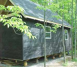 long wall of the cabin with two windows in, sitting up on its concrete piers