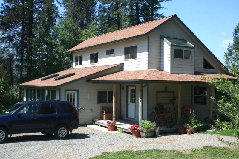 two story saltbox house with pale gray siding and dark green trim, a shed roofed porch across the front on peeled log posts and a pop-out bedroom alcove above