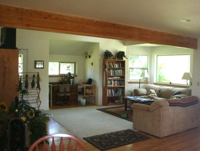 living room under an exposed beam, with a bay window, a bookcase and a desk set into the alcove beyond