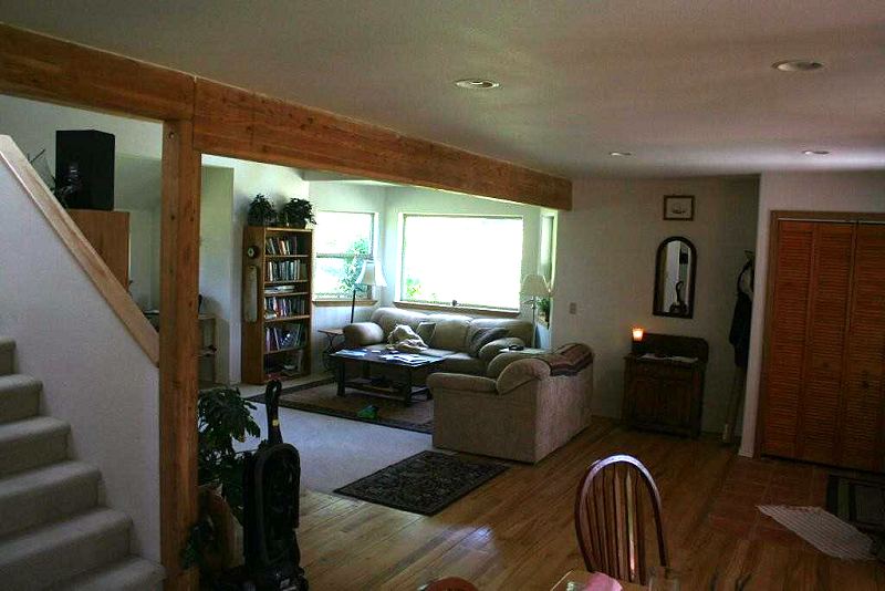 living room seen past the stair and a timber post, with the bay window and sofa at the far end