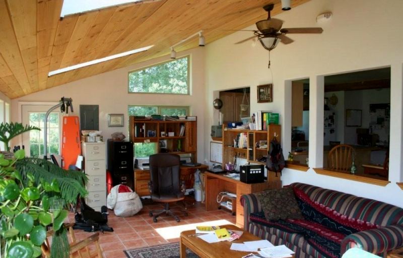 sunroom with a sloped wood ceiling, skylights, a tile floor, a desk and file cabinets along one wall and interior windows into the kitchen