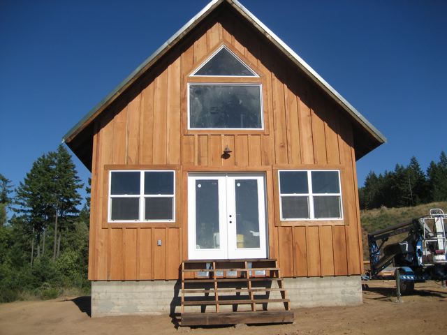 gable front of the finished cottage in board and batten redwood siding, with french doors