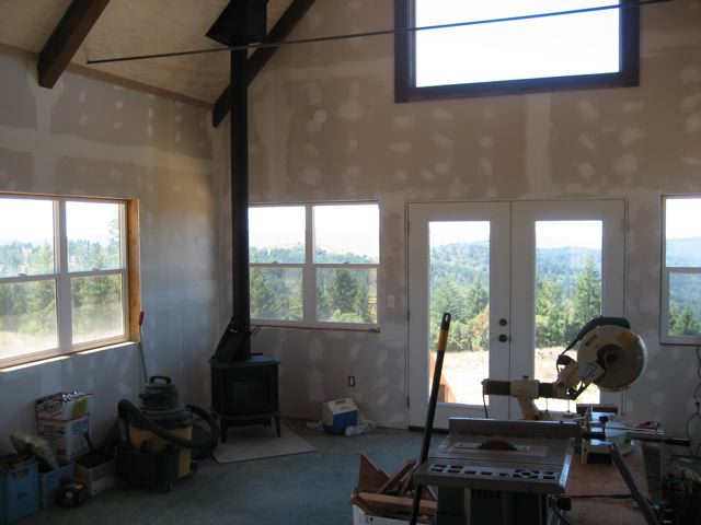 main room with drywall up, the woodstove and stove pipe in place, windows out to the ridge
