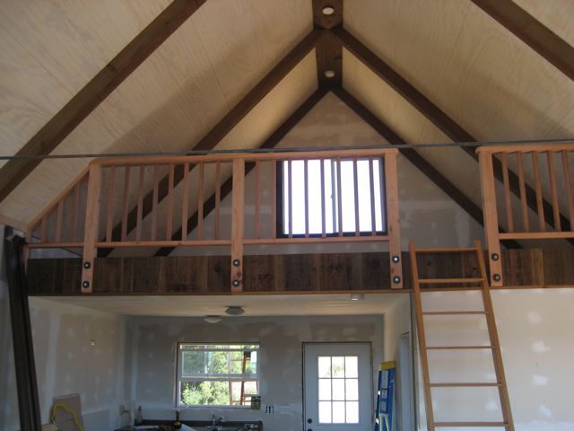 the finished loft behind a wood railing, with a ladder up to it and the ceiling boarded