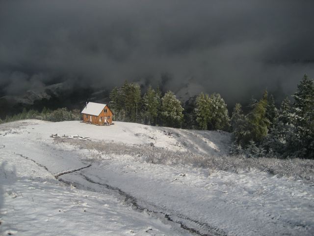 the cottage standing in fresh snow with a storm sky over the ridges behind